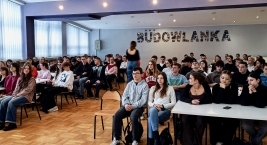 Duża grupa ludzi siedzi przy stołach w klasie, uczestnicząc w zajęciach edukacyjnych