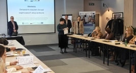 Osoby zgromadzone przy stołach w pomieszczeniu, uczestniczące w dyskusji.