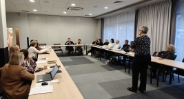 Grupa ludzi siedzi przy stołach w sali konferencyjnej, prowadząc dyskusję.