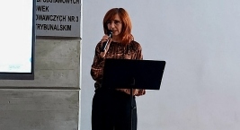 Kobieta wygłasza przemówienie z mównicy, z ekranem w tle