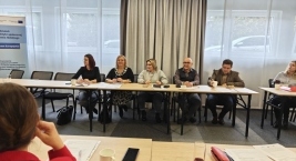 Uczestnicy spotkania siedzą przy stołach w przestronnej sali.