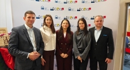 Grupa pięciu ludzi prezentuje się przed banerem z logo