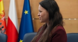 Kobieta w garniturze przemawia przy tym gestykulując. 