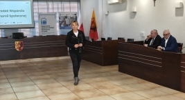 Kobieta w trakcie spotkania grupowego, stojąca przed dużym ekranem